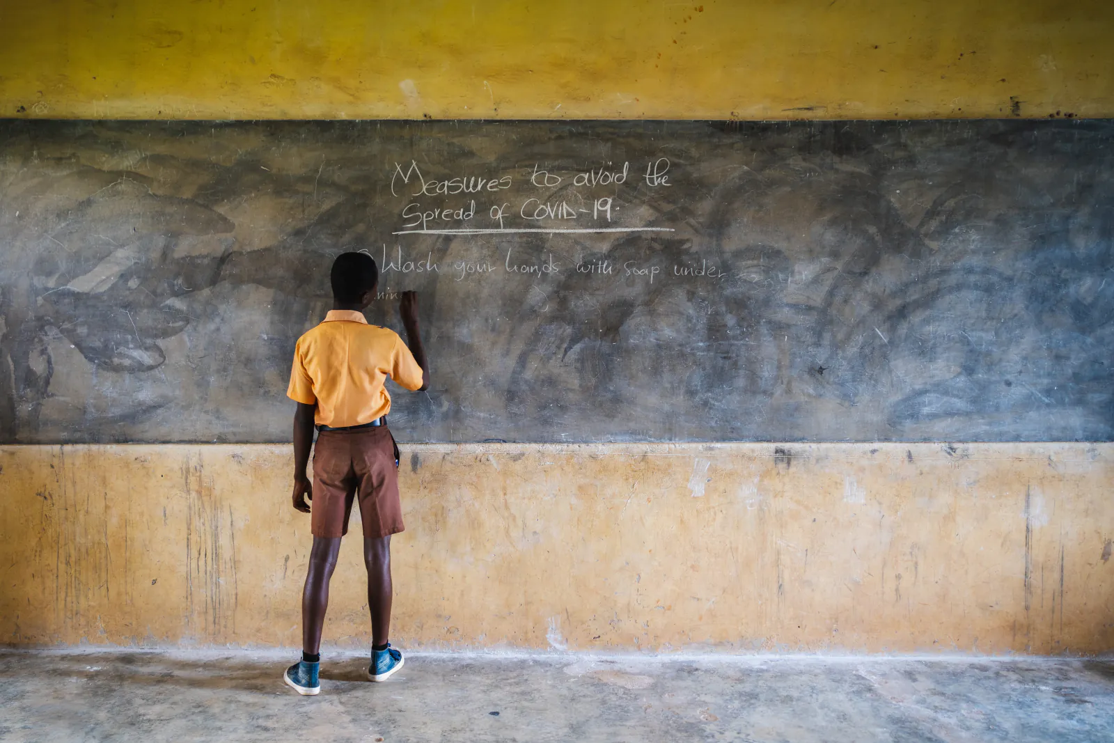 A student writes COVID-19 prevention measures on a classroom chalkboard — UNICEF WASH project, Ghana, photographed by Engman Wulff